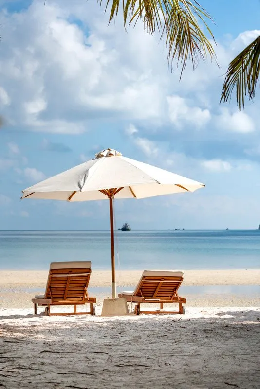 A white beach umbrella and two wooden loungers on the sand facing a calm sea