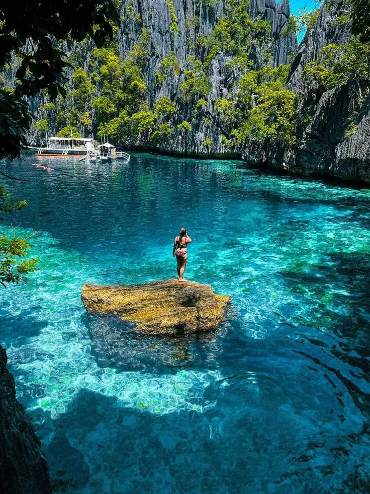 A swimmer standing on a rock in a turquoise lagoon framed by limestone cliffs in Coron