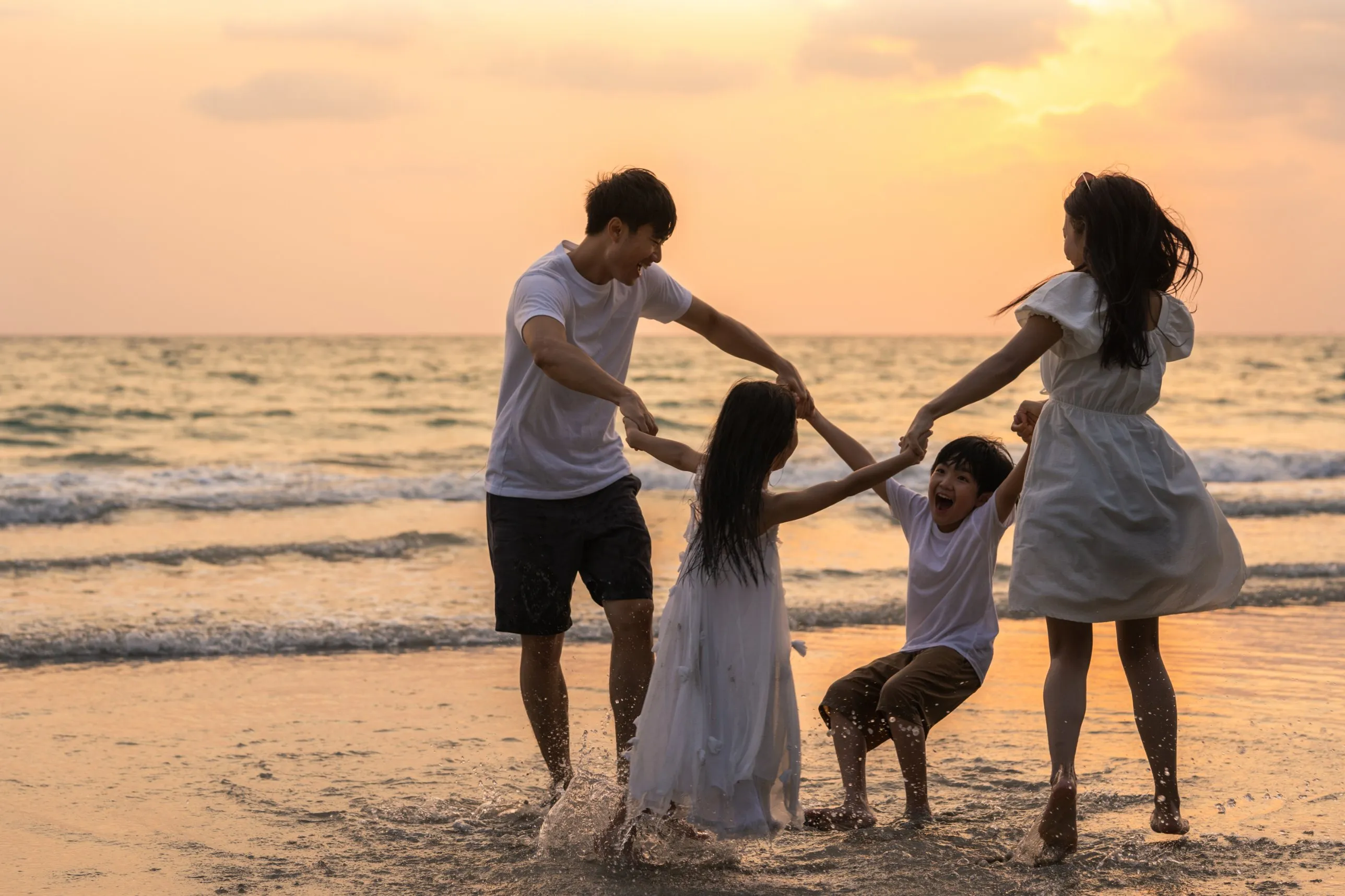 A family holding hands and dancing in the shallows of a beach at sunset
