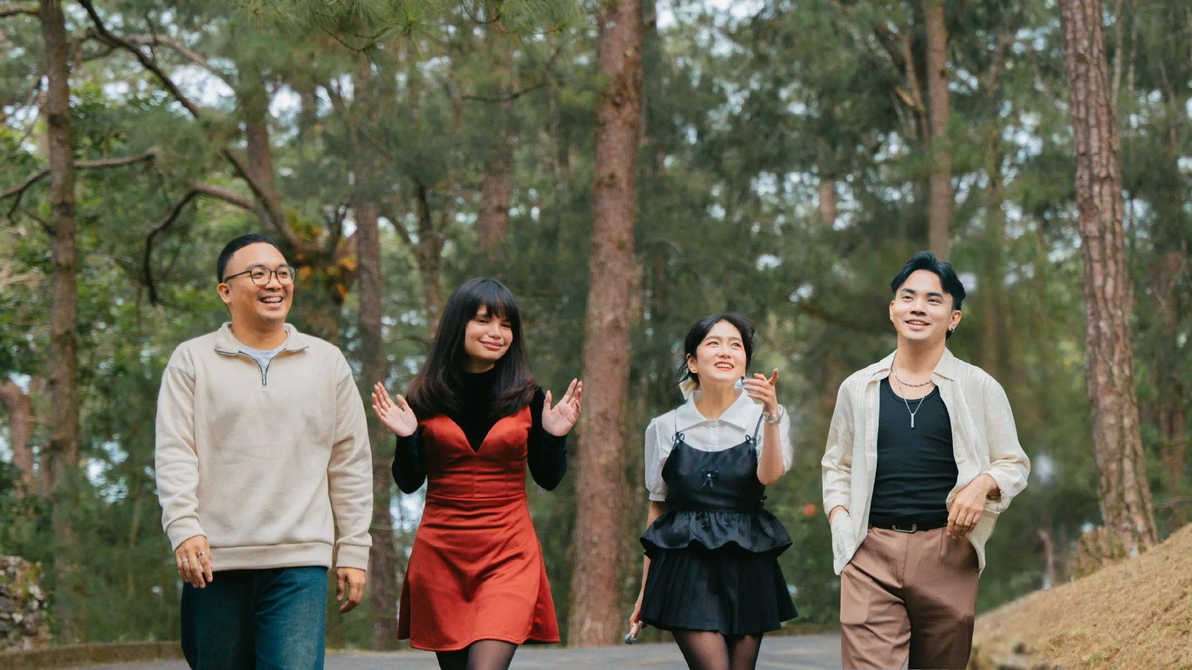 Four friends laughing as they walk together through a pine forest