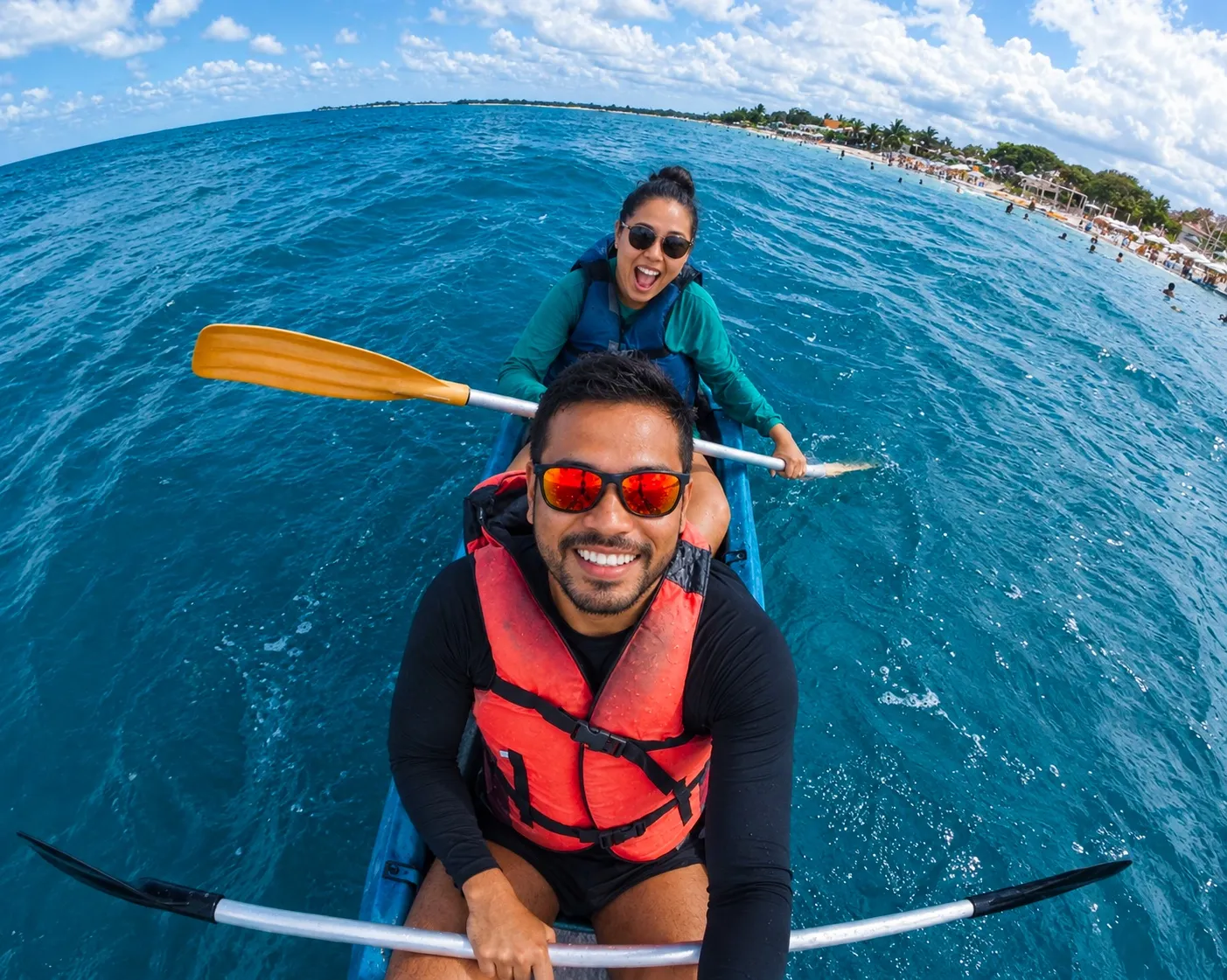 A smiling couple paddling a kayak across clear blue water